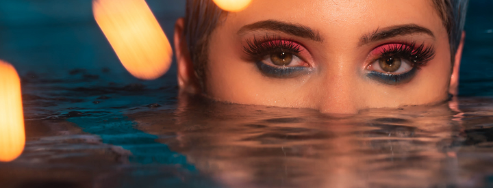 Woman with most of her face submerged under water except her eyes looking at you
